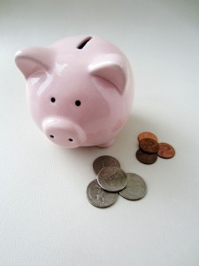 A ceramic piggy bank with two small piles of change next to it.