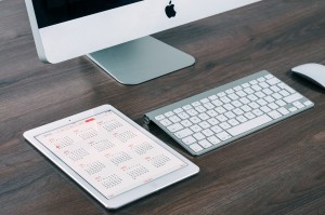 An Apple desktop computer and tablet on a wooden work desk. 