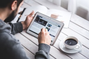 Man with coffee using tablet with stylus to browse the web.