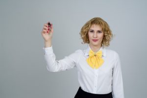 A woman in business clothes holding up a marker.